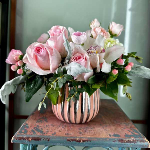 Pink roses and white blooms arranged in a striped vase