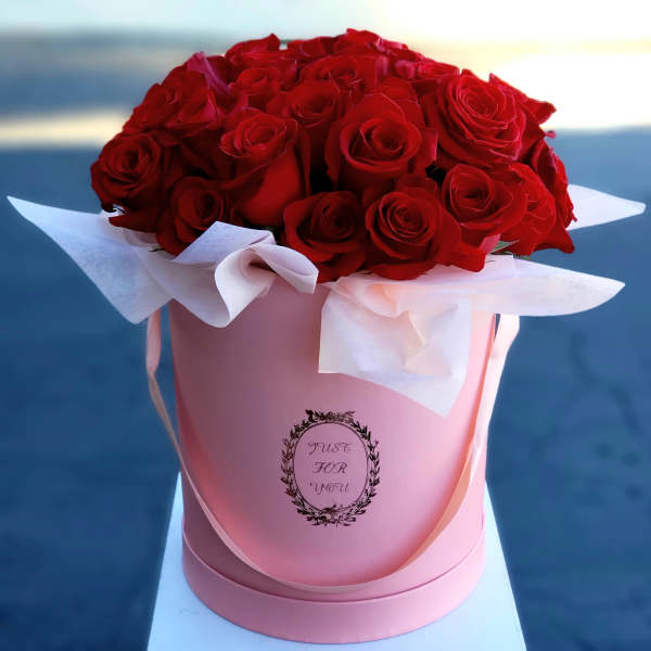 Red roses arranged in a pink hatbox with white tissue paper
