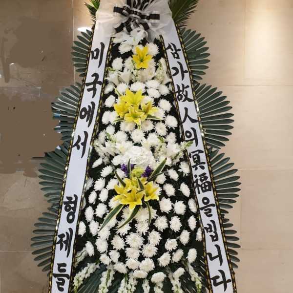Standing funeral wreath with white and yellow flowers and Korean condolence ribbons