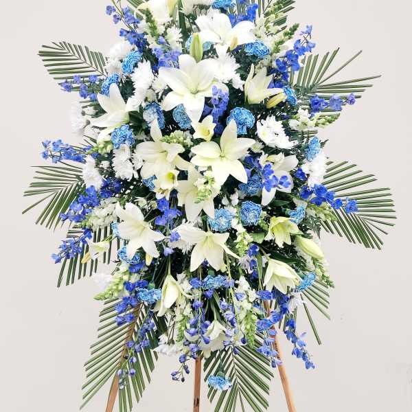 Standing floral spray with white lilies and blue flowers on an easel