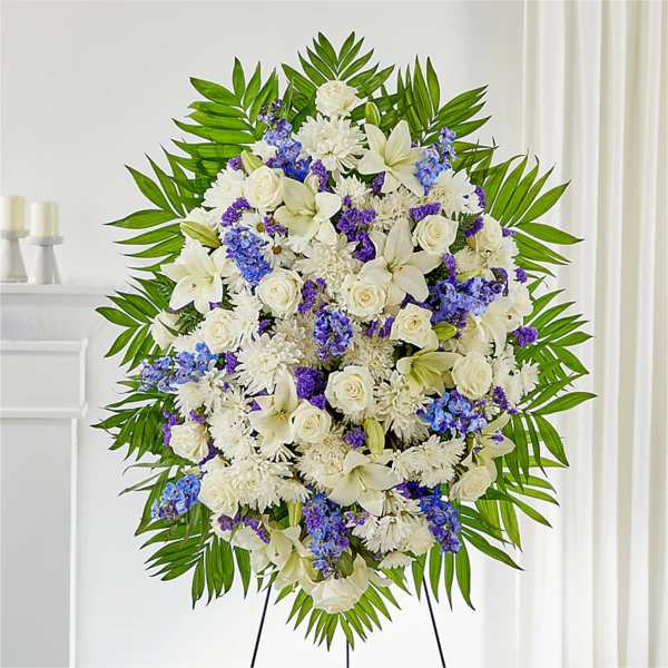 Large standing floral spray with white and blue flowers on a green palm backdrop