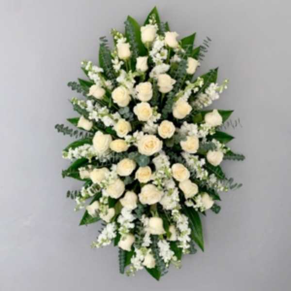 Oval spray of white roses and white flowers arranged over dark foliage