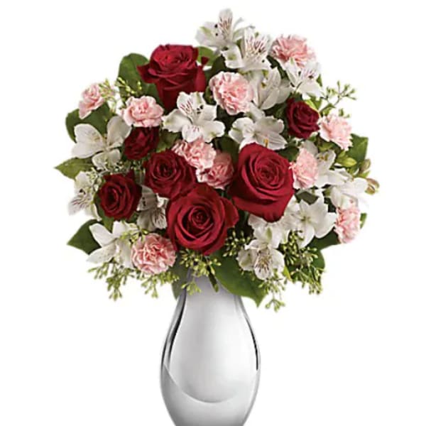 Red roses, pink carnations, and white alstroemeria in a glass vase