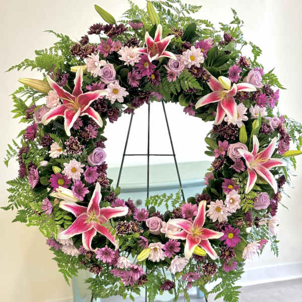 Circular floral wreath with pink lilies and purple blooms on a stand