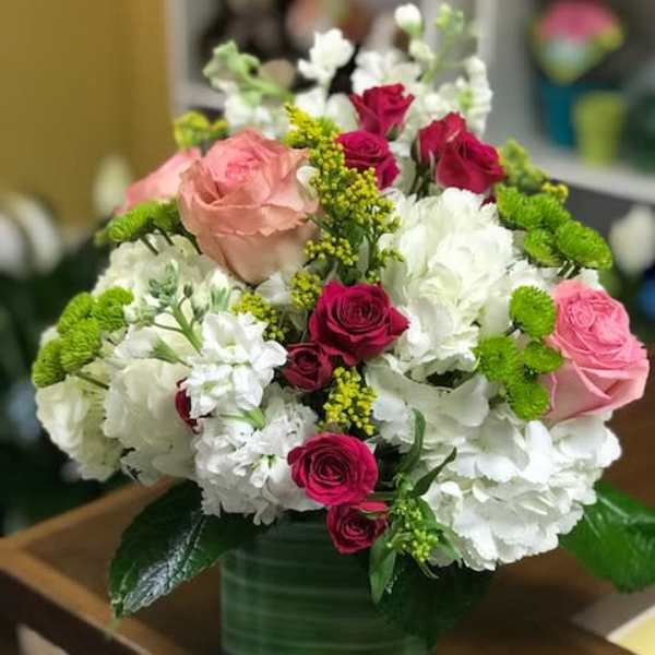 Round arrangement of white hydrangeas with pink and red roses in a green glass cube vase