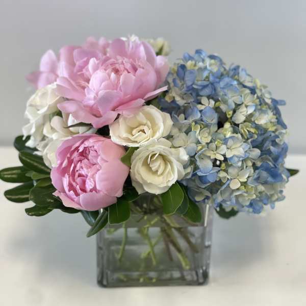 Pink peonies, white roses, and blue hydrangeas in a square glass vase