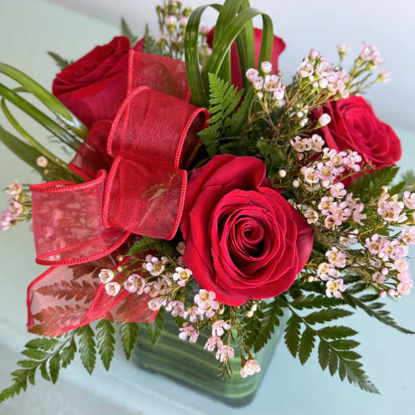 Red roses with pink filler flowers and a red ribbon in a glass vase