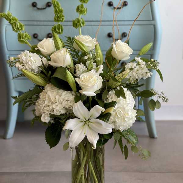 White floral arrangement in a clear glass vase with lilies and roses