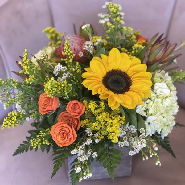 Bouquet with a sunflower, orange roses, and white hydrangea in a square vase
