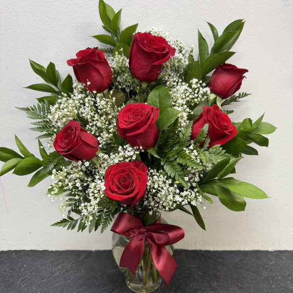 Red roses arranged in a clear glass vase with a burgundy ribbon
