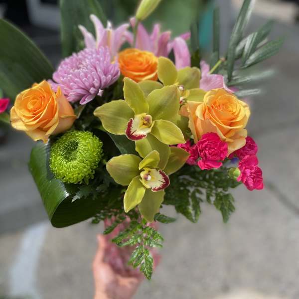Handheld bouquet with orange roses, pink lilies, and green orchids