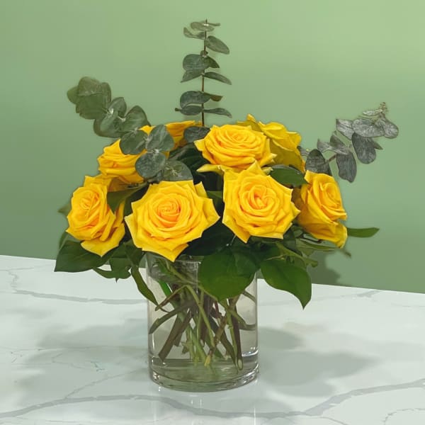 Yellow roses arranged in a clear glass vase with eucalyptus foliage