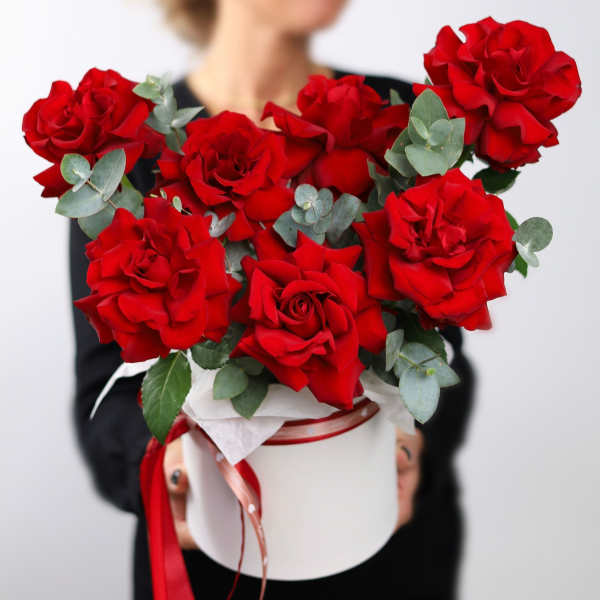 Red roses arranged in a white hat box with eucalyptus and ribbon