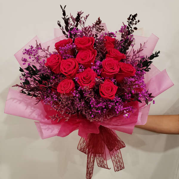 Bouquet of red roses with purple filler flowers wrapped in pink paper