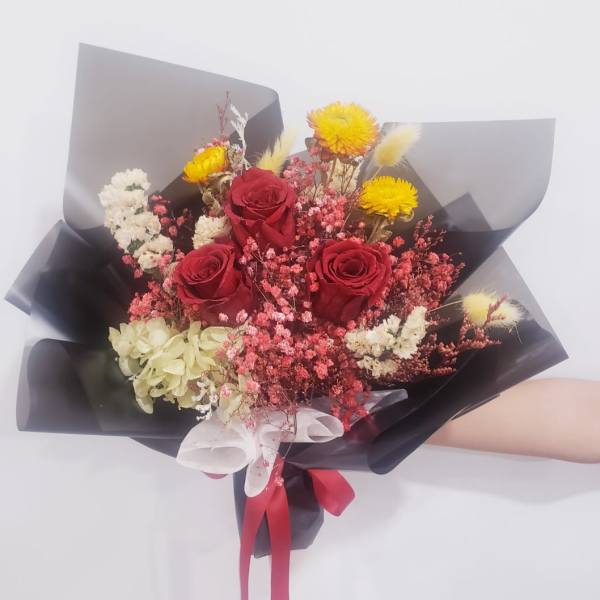 Bouquet of red roses with yellow and white filler flowers wrapped in black paper