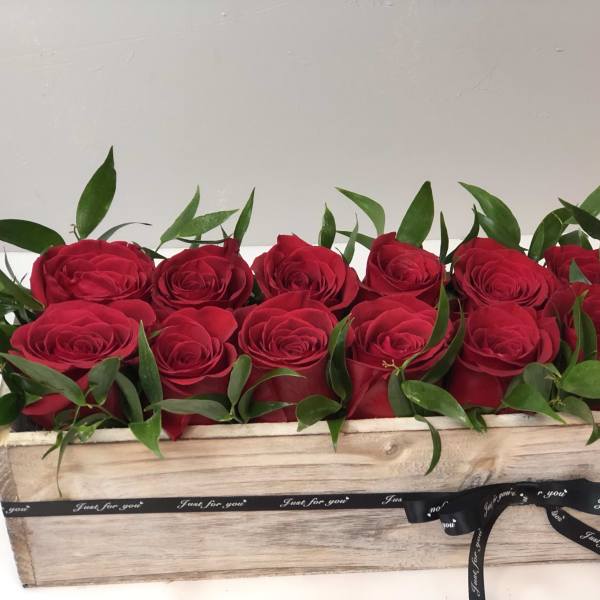 Red roses arranged in a wooden box with a black ribbon
