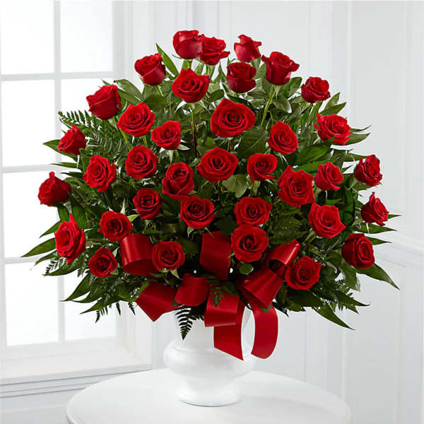 Red roses arranged in a white vase with a red ribbon
