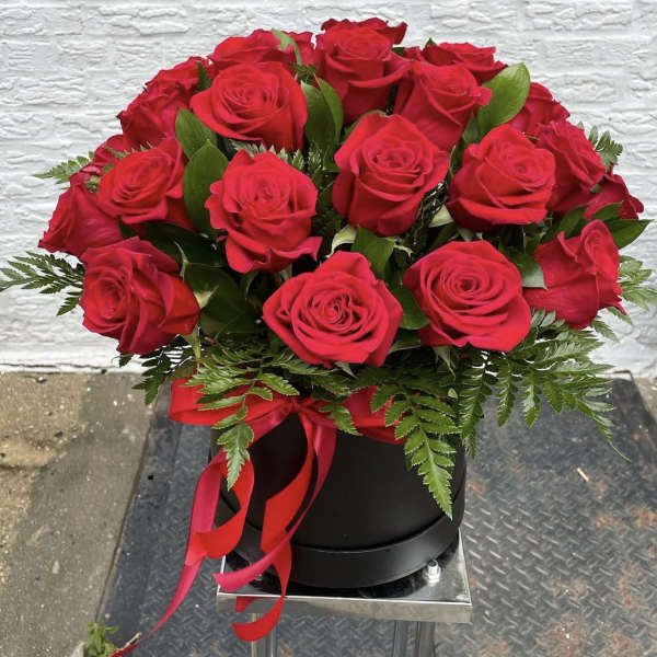 Red roses arranged in a black hatbox with a red ribbon