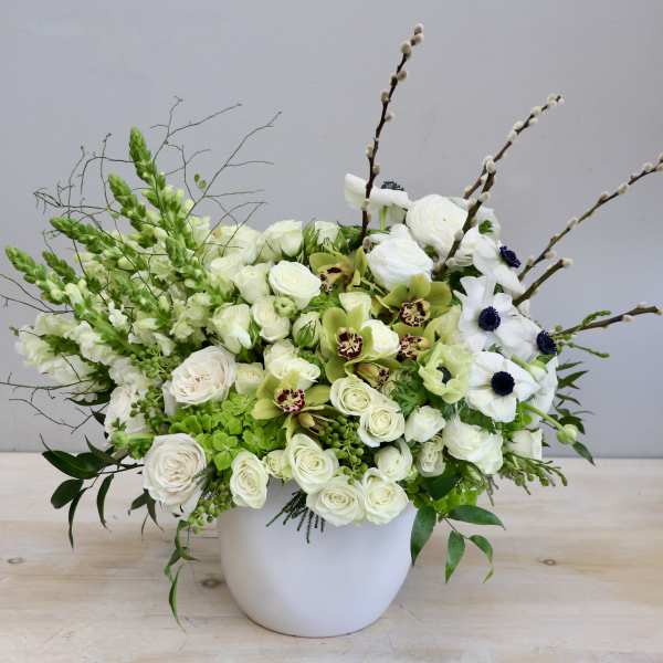 Asymmetrical white and green floral arrangement in a white ceramic pot