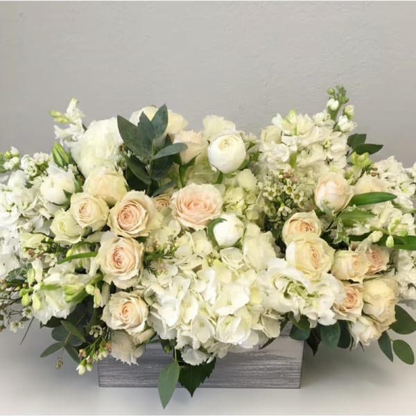 Low white and cream flower arrangement with roses and hydrangeas in a rectangular wooden box