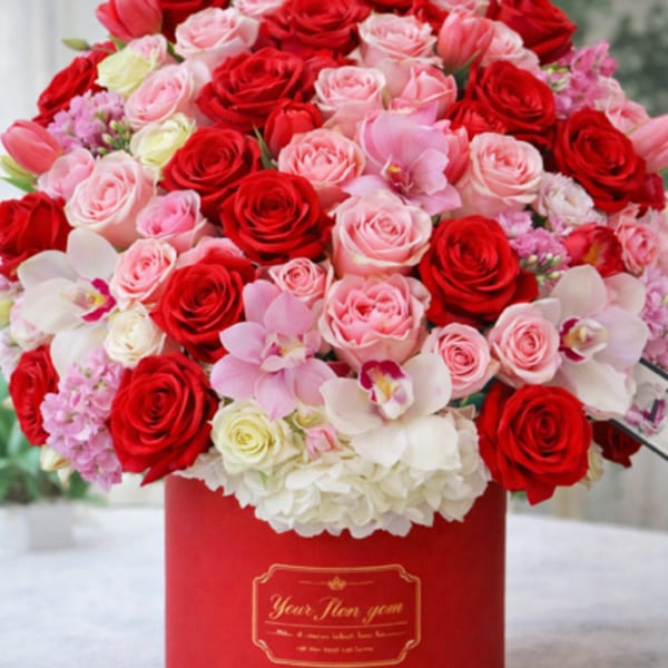 Red and pink roses with orchids in a red hat box