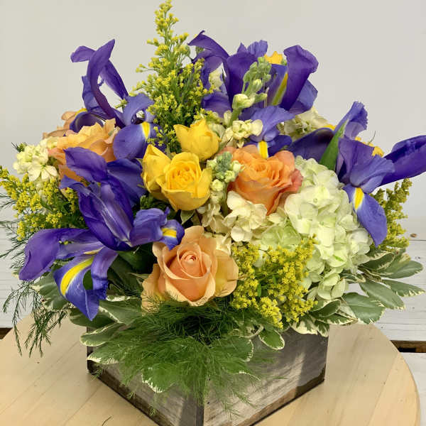 Mixed bouquet of purple irises, roses, and hydrangeas in a wooden box