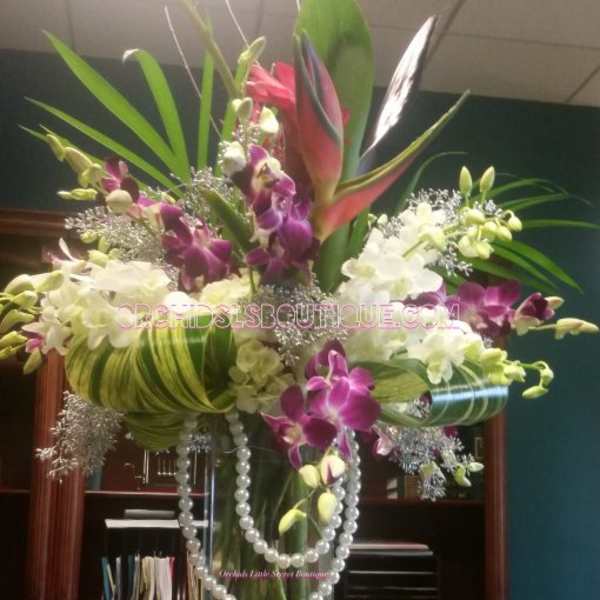 Tall orchid arrangement in a clear glass vase with pearl strands
