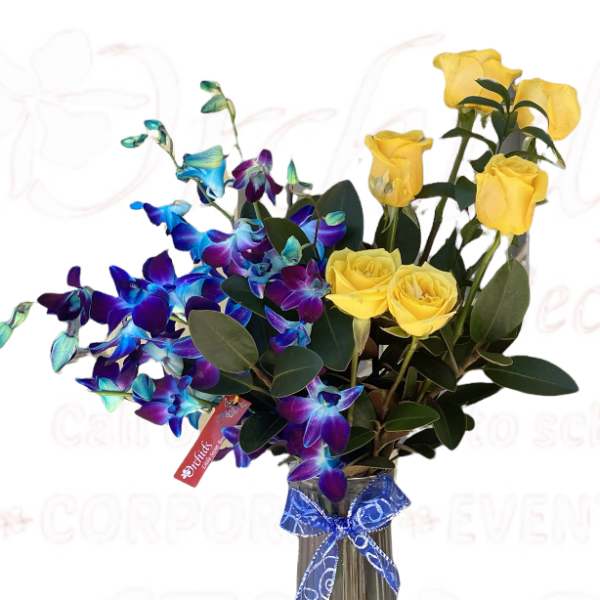 Yellow roses and blue orchids in a glass vase with a blue ribbon.