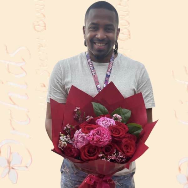 Man holding a bouquet of red and pink roses wrapped in burgundy paper