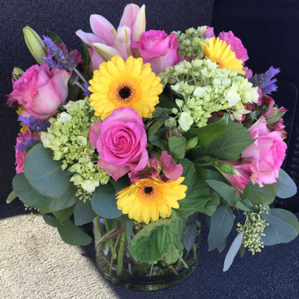Bouquet of pink roses, yellow gerbera daisies, and lilies in a glass vase