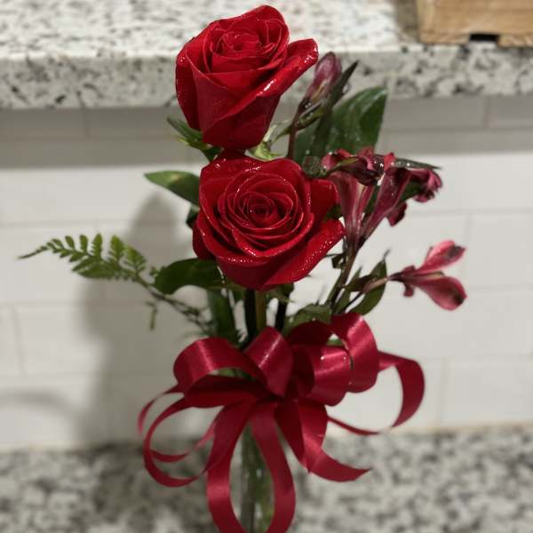 Two red roses with pink alstroemeria in a glass vase tied with a red ribbon.