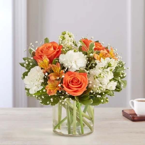 Orange roses and white flowers in a clear glass vase