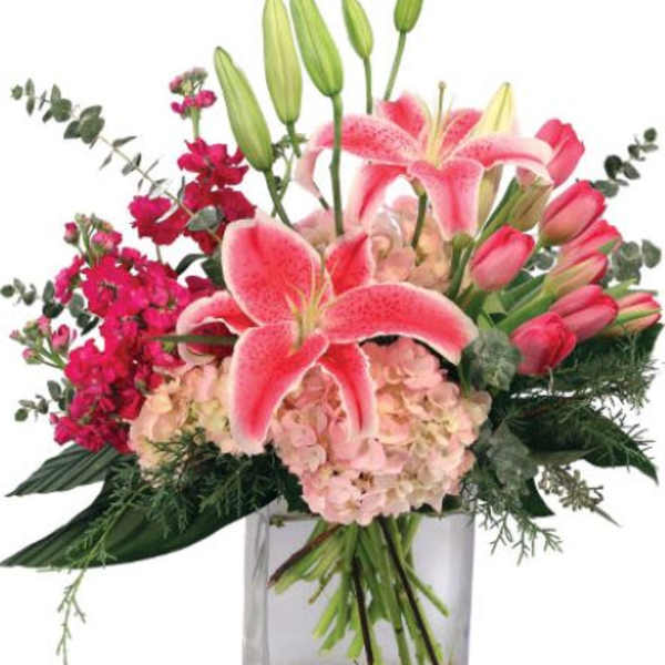 Pink lilies, hydrangeas, and tulips arranged in a clear rectangular glass vase