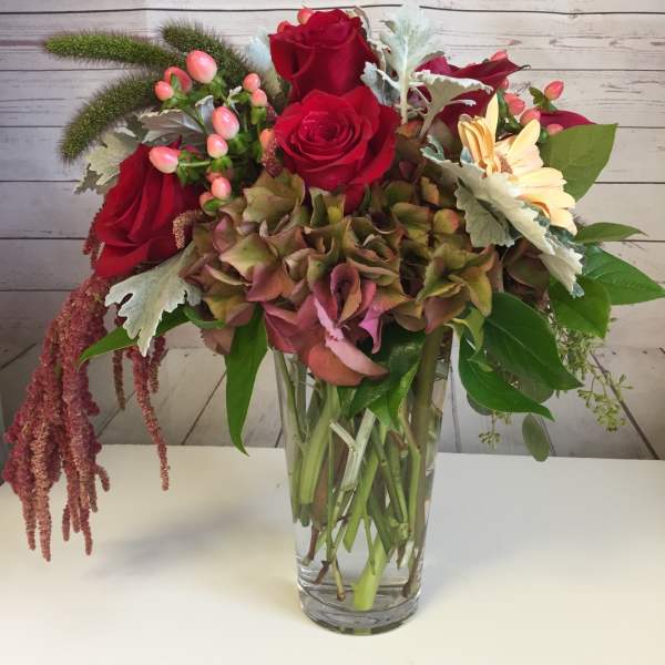 Red roses and mixed blooms in a clear glass vase