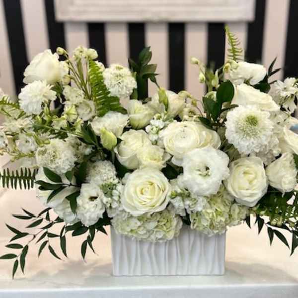 Low white flower arrangement with roses and mixed blooms in a rectangular white vase