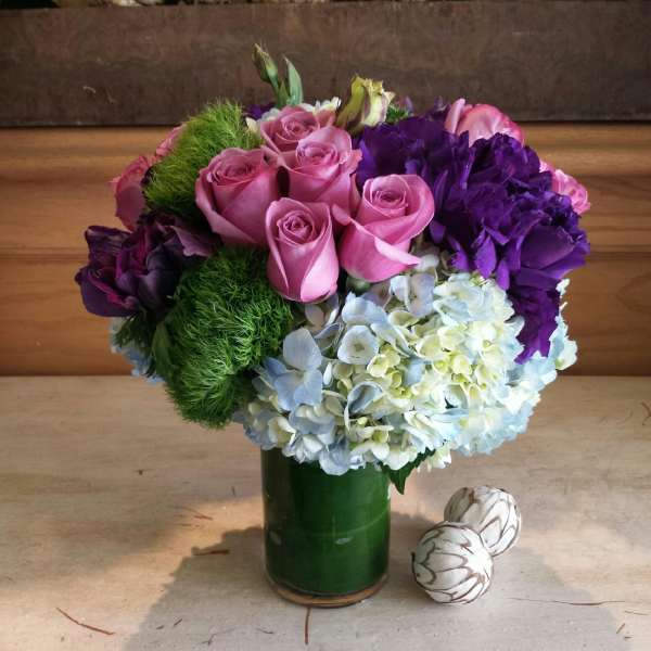 Pink roses and purple hydrangeas in a green vase with two decorative eggs