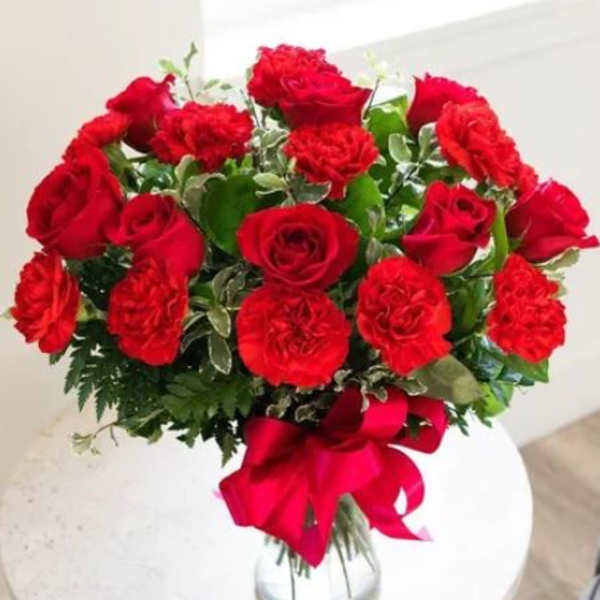 Bouquet of red roses and carnations in a glass vase with a red ribbon
