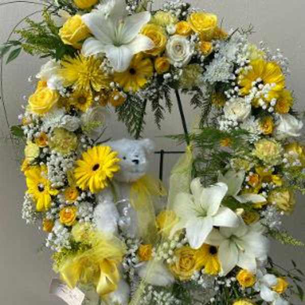 Yellow and white floral wreath on a stand with a teddy bear in the center