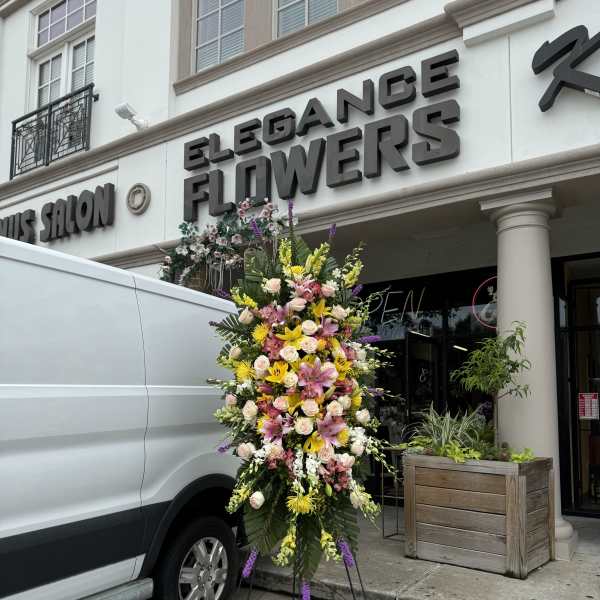 Tall standing floral spray with pink, yellow, and white flowers on a metal easel.