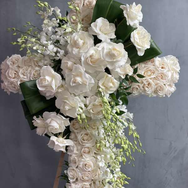 Large cross-shaped floral arrangement of white and blush roses with cascading orchids
