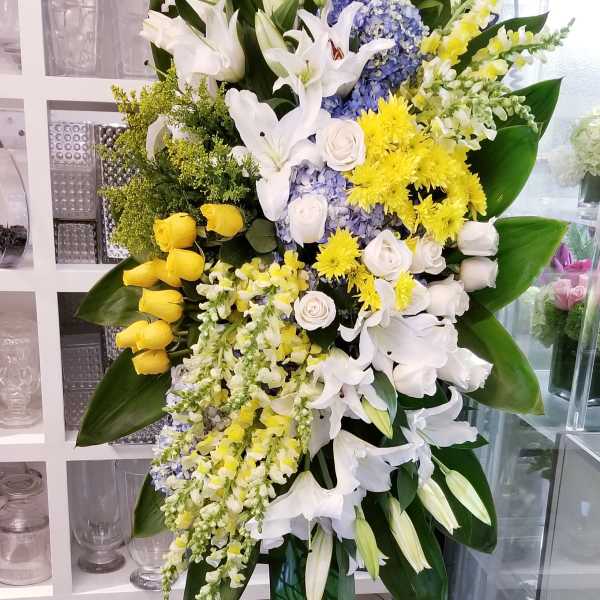 Large standing floral spray with white lilies, yellow roses, and blue hydrangeas