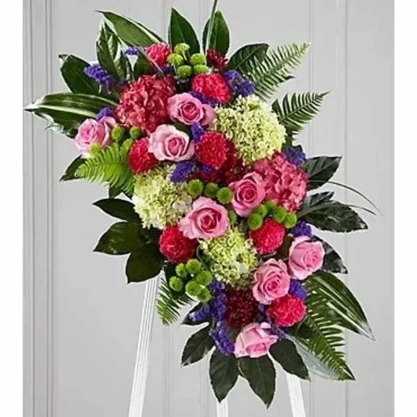 Standing floral spray with pink roses and mixed blooms on a white easel