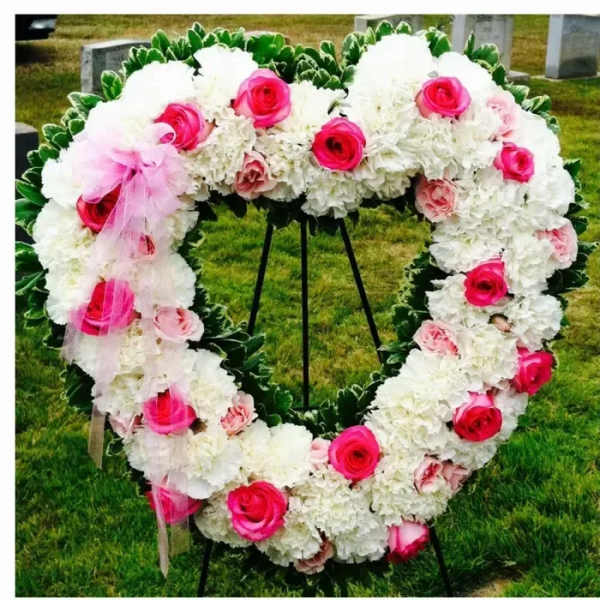 Heart-shaped floral wreath with white blooms and pink roses on a stand