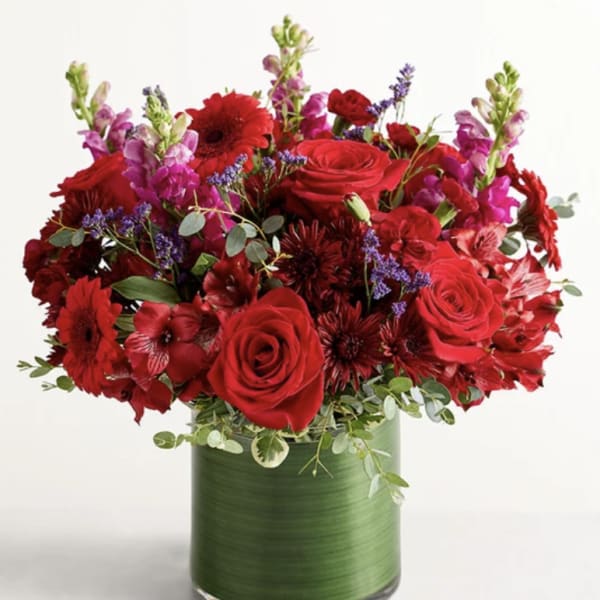 Red roses and mixed flowers arranged in a green glass vase