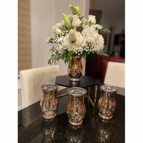 White floral arrangement in a gold vase with three matching votive holders