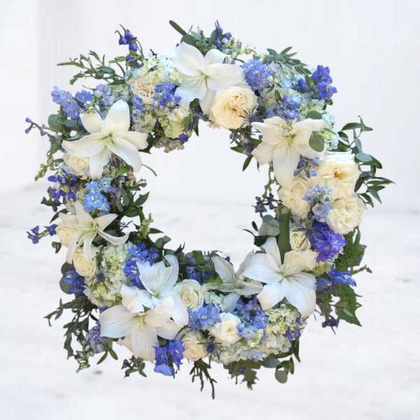 Floral wreath with white lilies, cream roses, and blue flowers