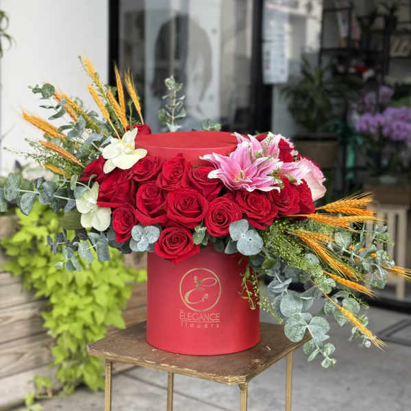 Red rose arrangement in a round hat box with lilies and wheat accents