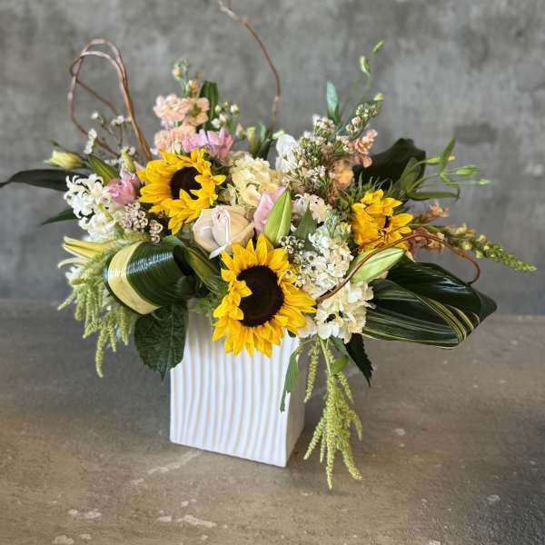 Mixed floral arrangement with sunflowers and roses in a white vase