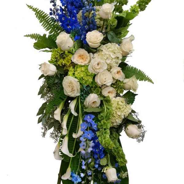 Tall standing floral spray with white roses, blue delphinium, and green accents