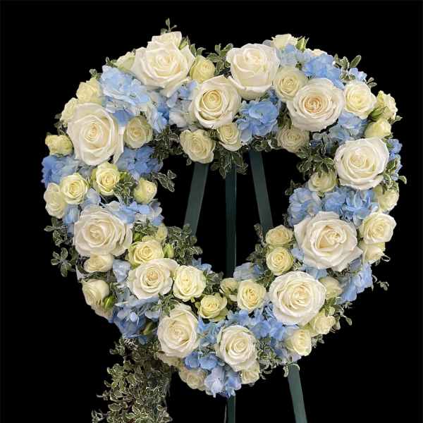 Heart-shaped floral wreath of white roses and blue hydrangeas on an easel
